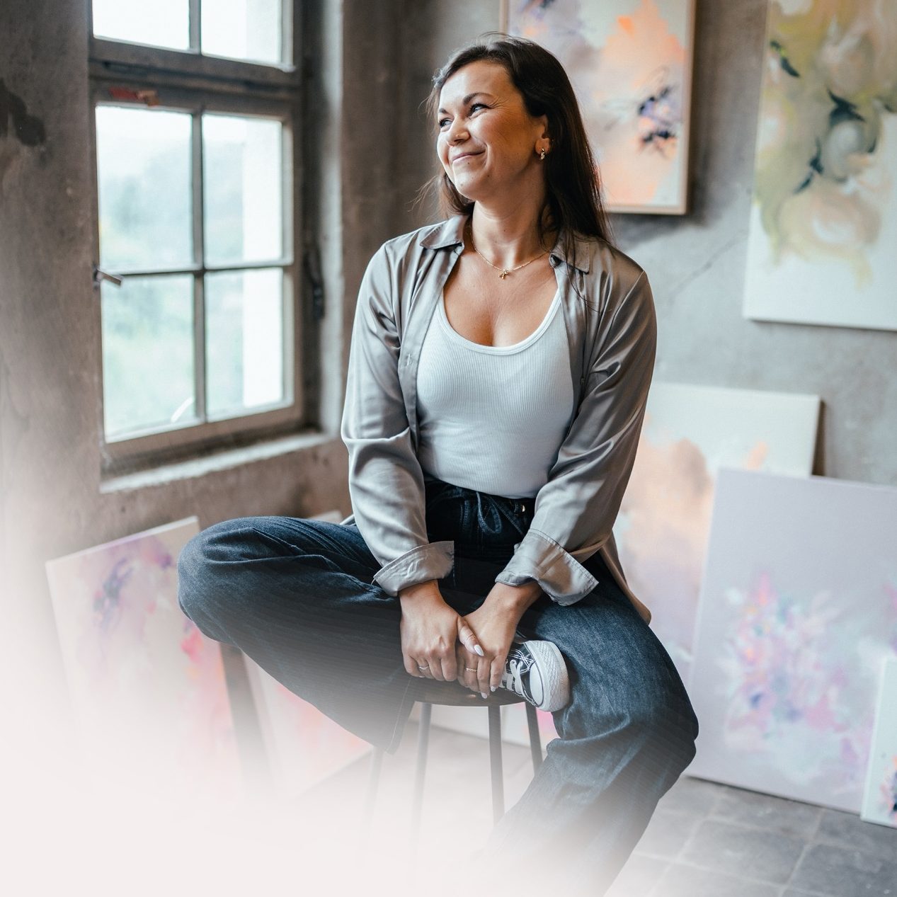 Künstlerin Anca Juliana Künstlerin Anca Juliana sitzt in einem Atelier zwischen abstrakten Gemälden.