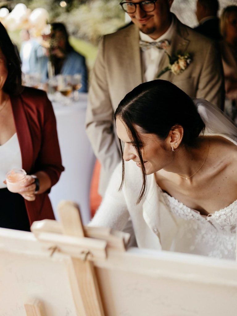 Wedding-Painting – Hochzeitsmalerei – Künstlerisches Gästebuch Eine Braut in einem eleganten Kleid, während sie an einem Kunstwerk malt.